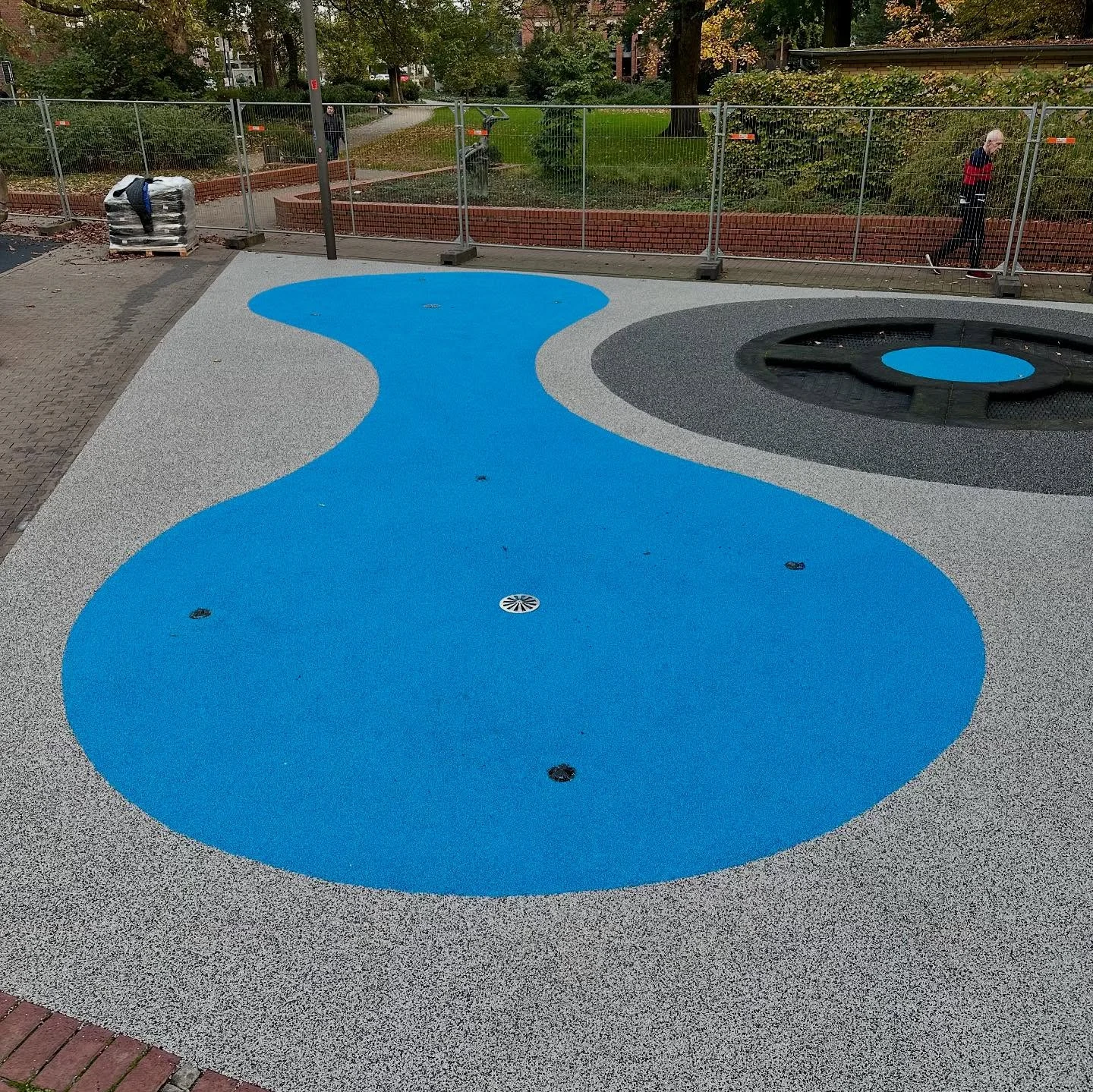 Frei geformte himmelblaue Fallschutzfläche, fugenlos in einen lichtgrauen Belag eingearbeitet