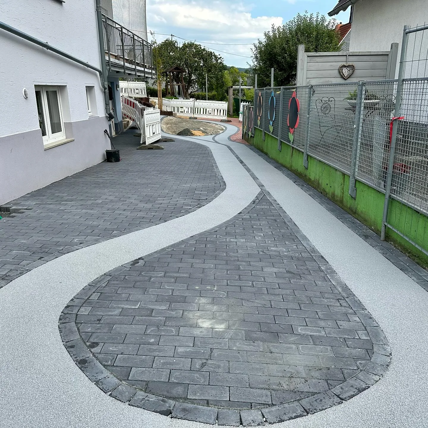 Lichtgrauer Fallschutzweg, nahtlos an Pflastersteine angeschlossen